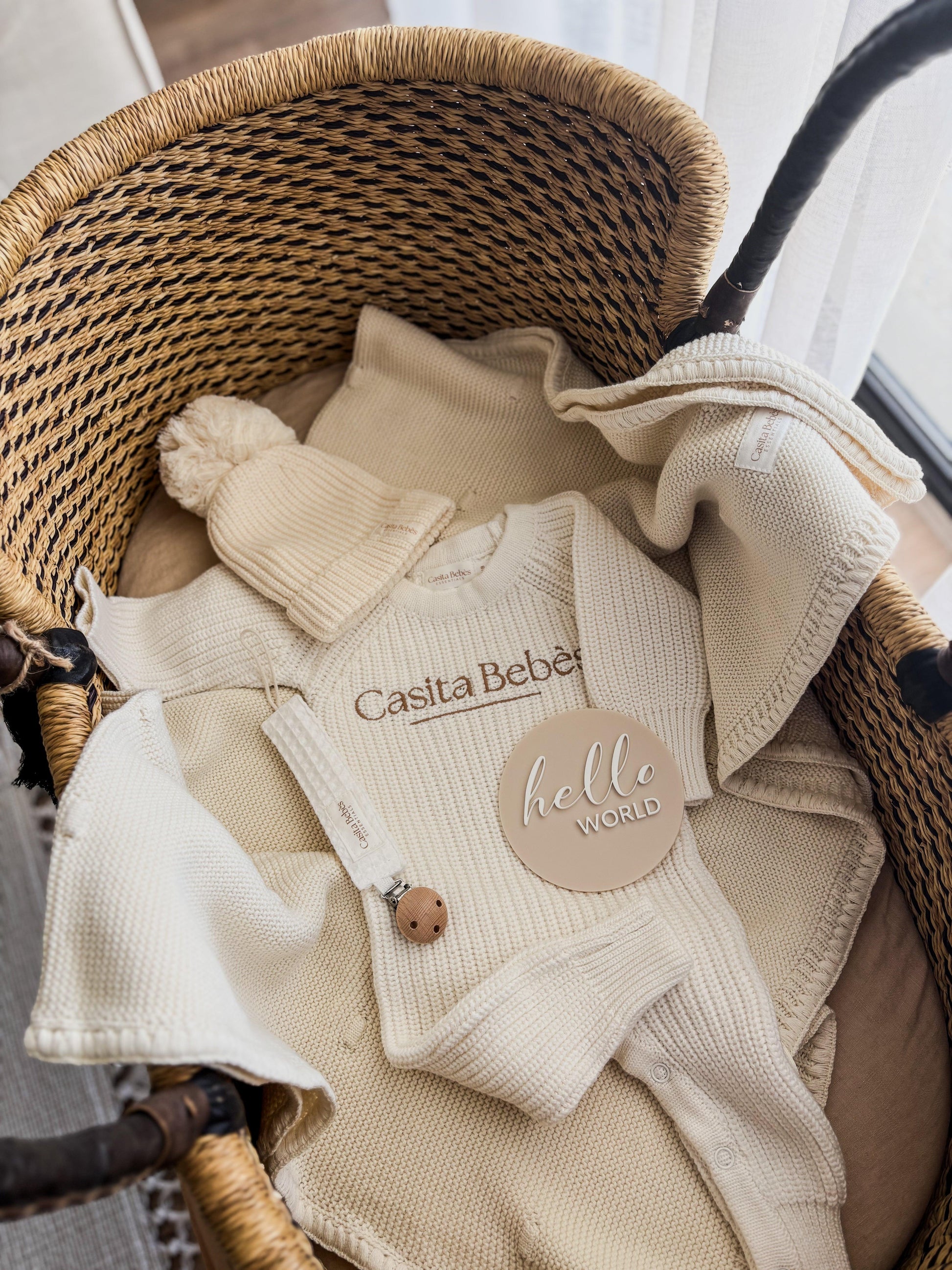 Organic baby onesie, knit hat, and blanket in wicker basket, 'hello world' tag, neutral nursery essentials