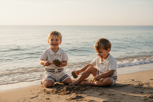 Two toddlers wearing organic cotton Swim Essentīals Tops Blanco playing on the beach sand.