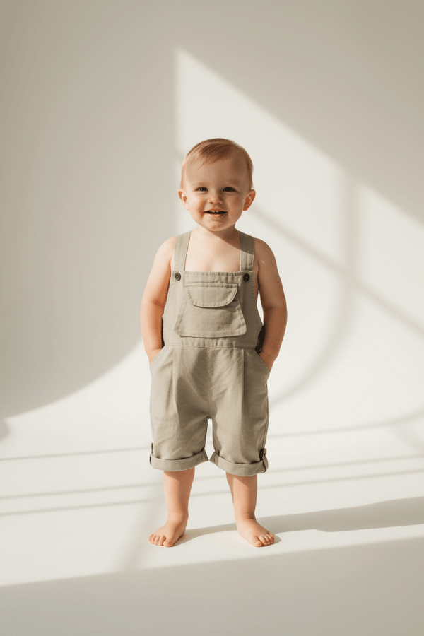 Baby in organic cotton overalls, smiling with soft sunlight