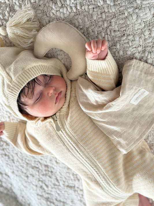Baby wearing beige knitted romper with hood, certified organic Casita Bebes baby clothing.