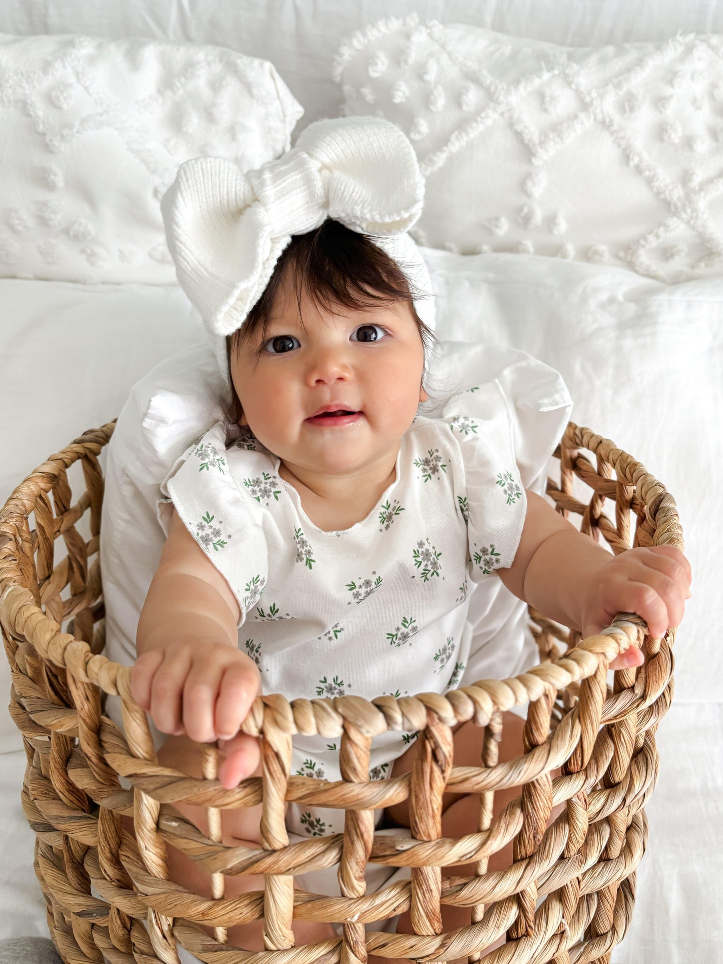 Organic certified baby bodysuit with floral print, worn by infant girl with white headband in woven basket.