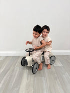 Two toddlers in striped organic baby pajamas riding a vintage-style ride-on toy car indoors
