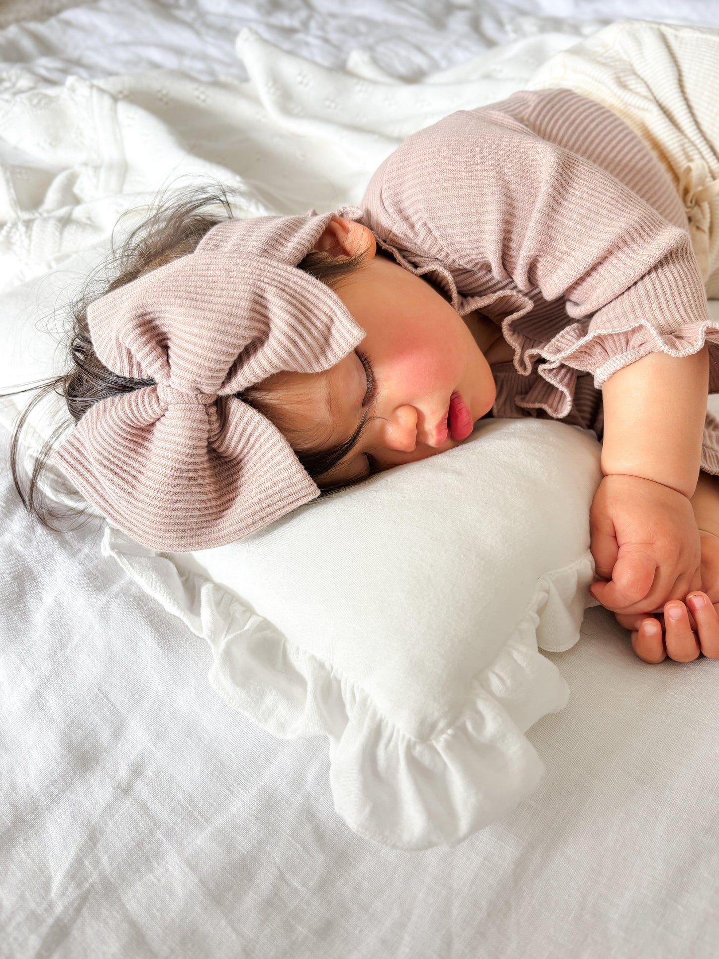 Sleeping baby wearing dusty pink ribbed organic cotton outfit with matching bow, Casita Bebes baby clothing.