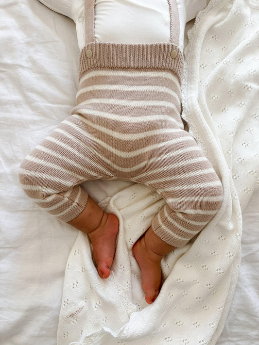 Organic knitted baby overalls in beige and white stripes on a sleeping baby.