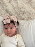 Baby wearing soft knit bow headband and organic onesie on cozy blanket