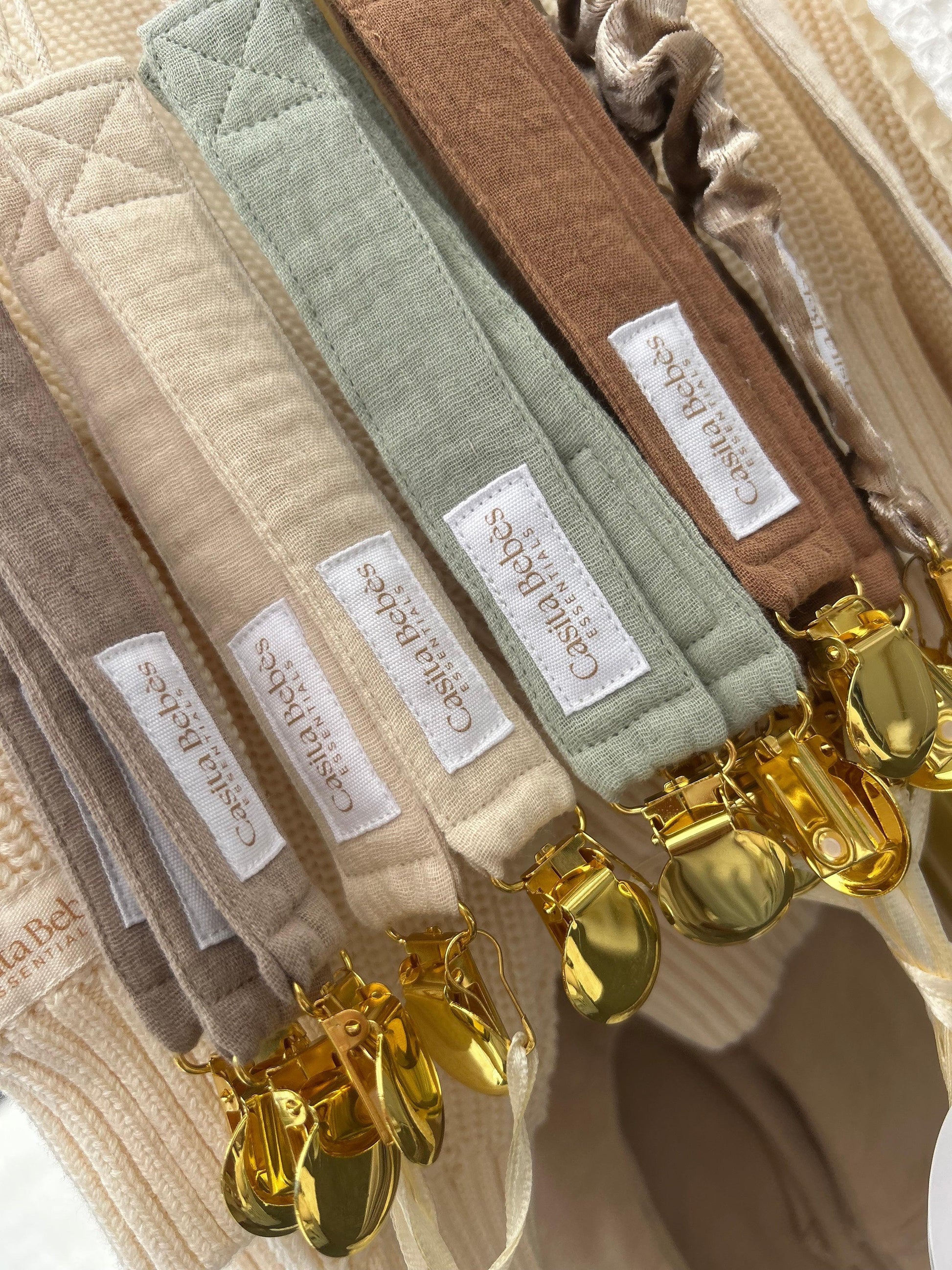 Certified organic Essentīals Gold Dummy Holders in dusty beige, brown, green, khaki with gold clips, close-up detail.