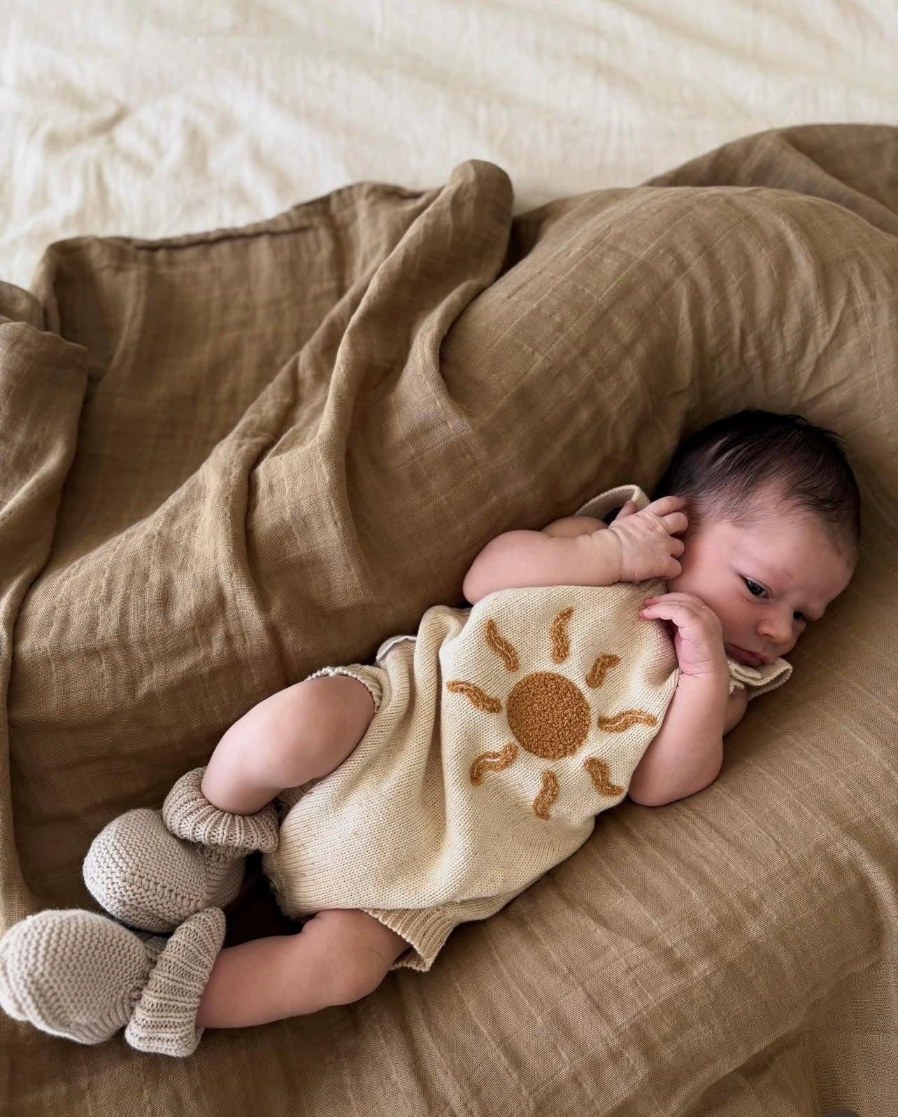 Newborn wearing organic muslin swaddle in dusty brown with sun print, certified organic baby clothing by Casita Bebes.