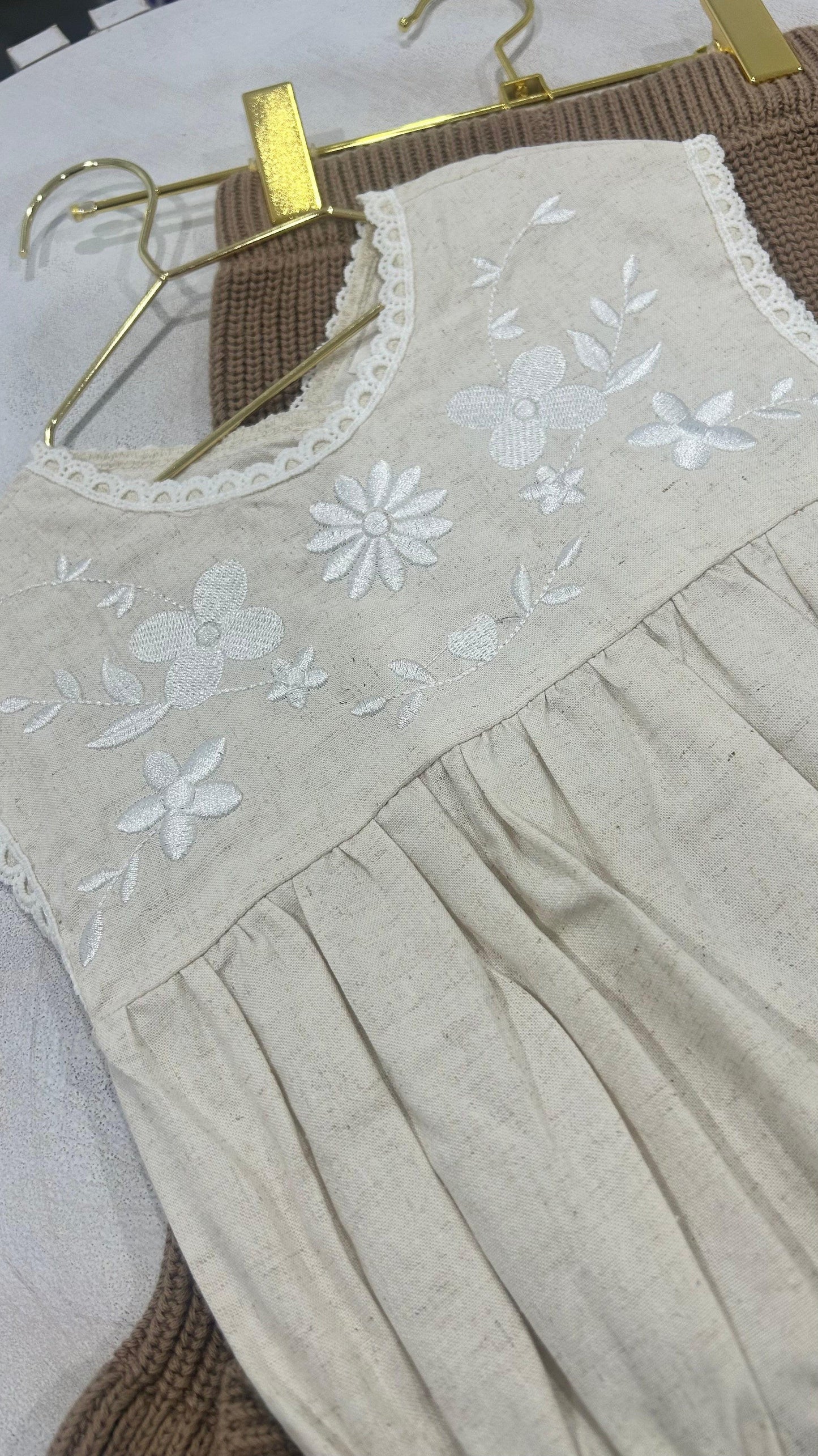 Organic beige cotton baby romper with white floral embroidery and scalloped neckline from Casita Bebes.