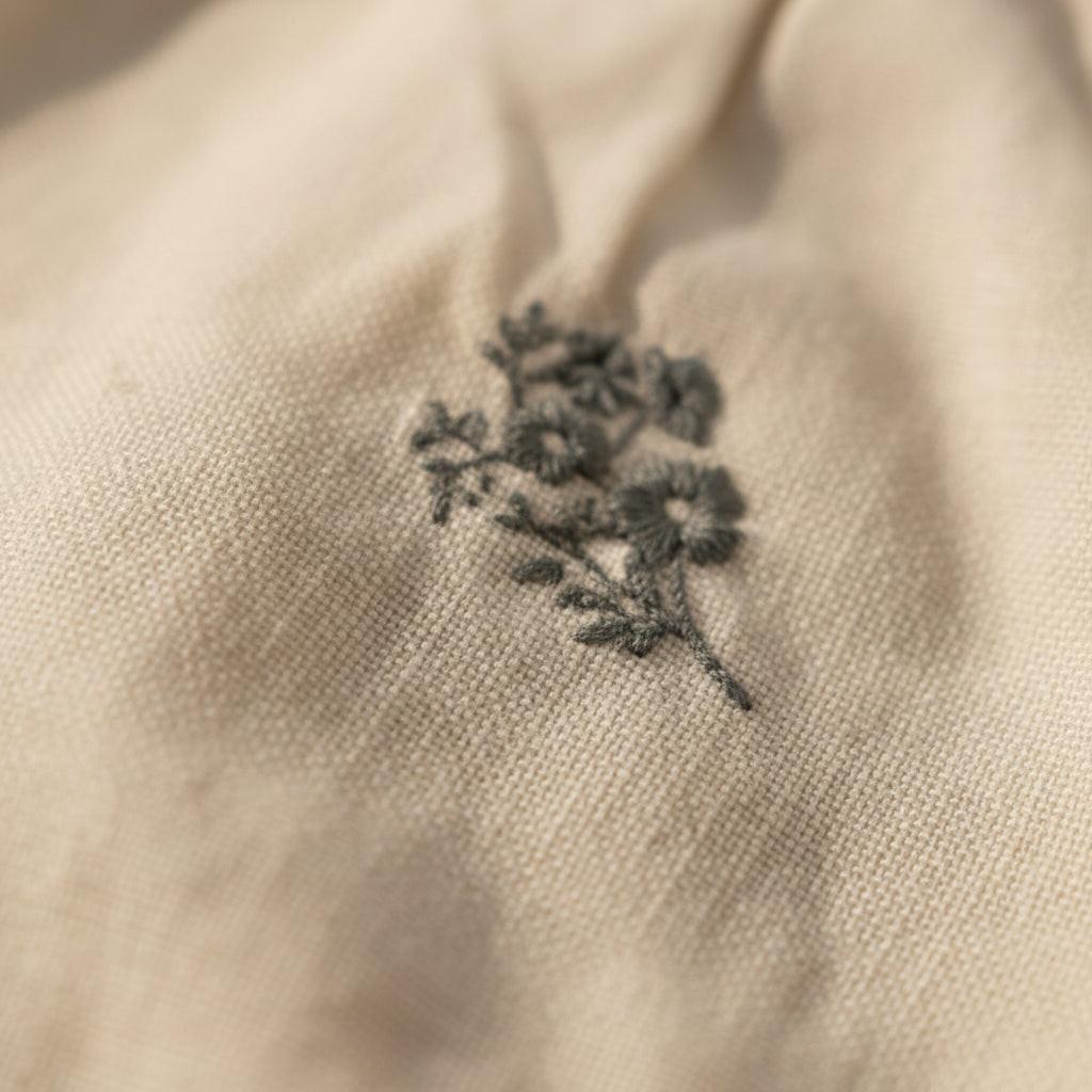 Close-up of certified organic beige baby romper with delicate gray floral embroidery from Casita Bebes.