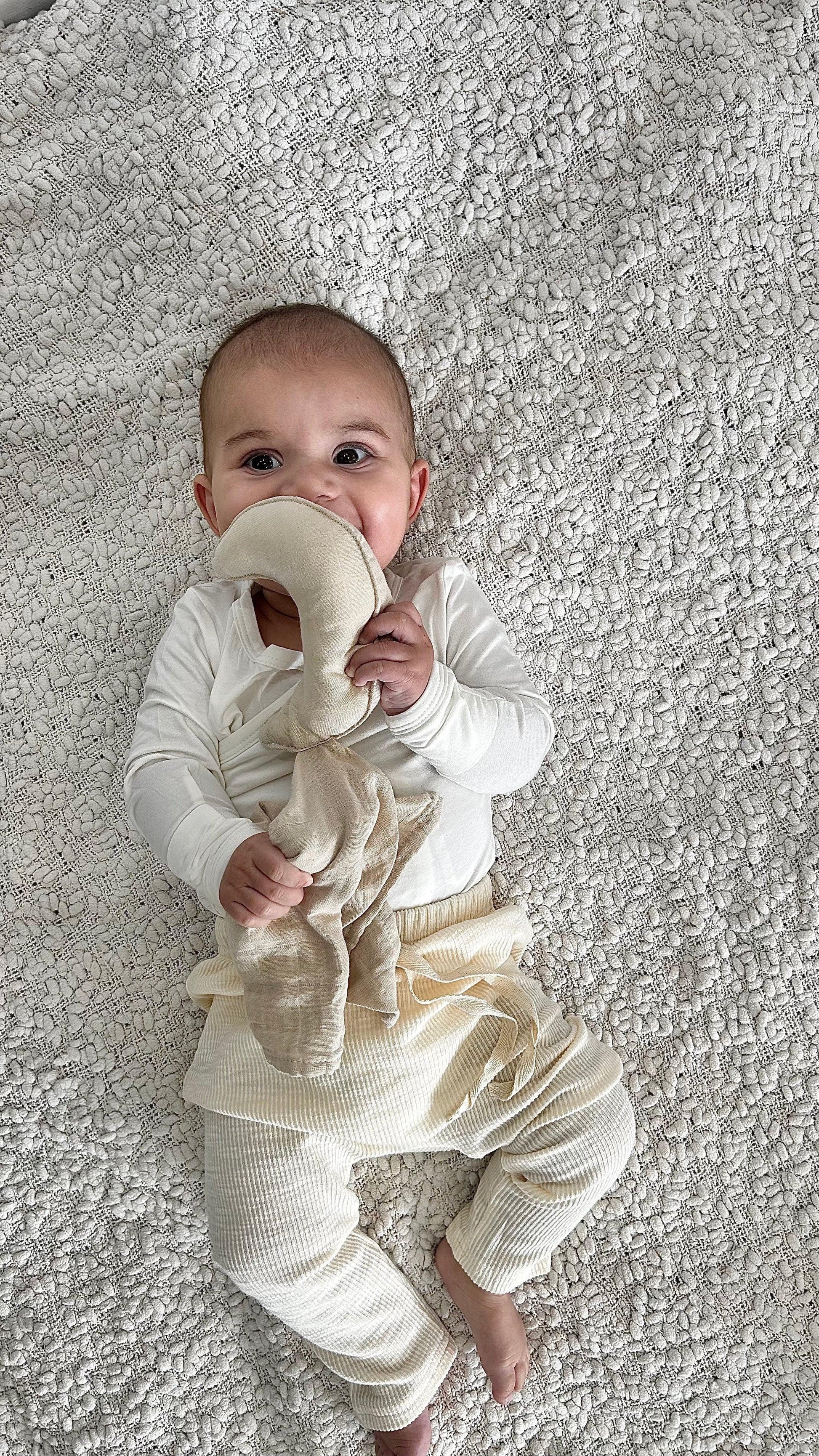 Baby wearing organic cotton Essentīals Cuddly Moon comforter on textured white blanket.