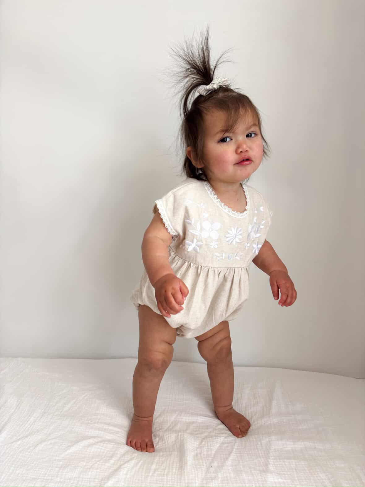 Organic cotton baby romper in cream with short sleeves and subtle embroidery, worn by toddler girl.