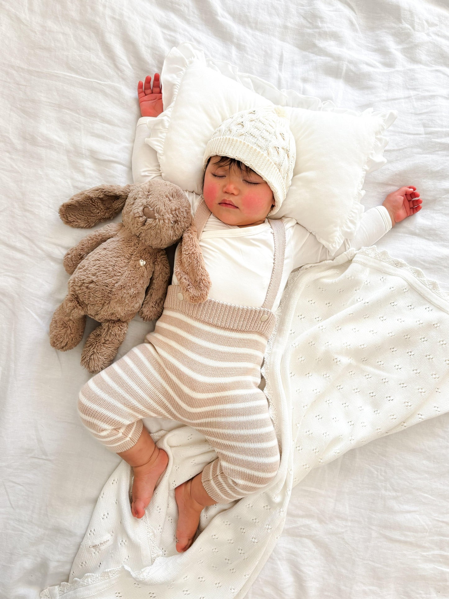 Baby wearing organic Casita Bebes knitted overalls in cream and beige stripes, certified organic baby clothing.