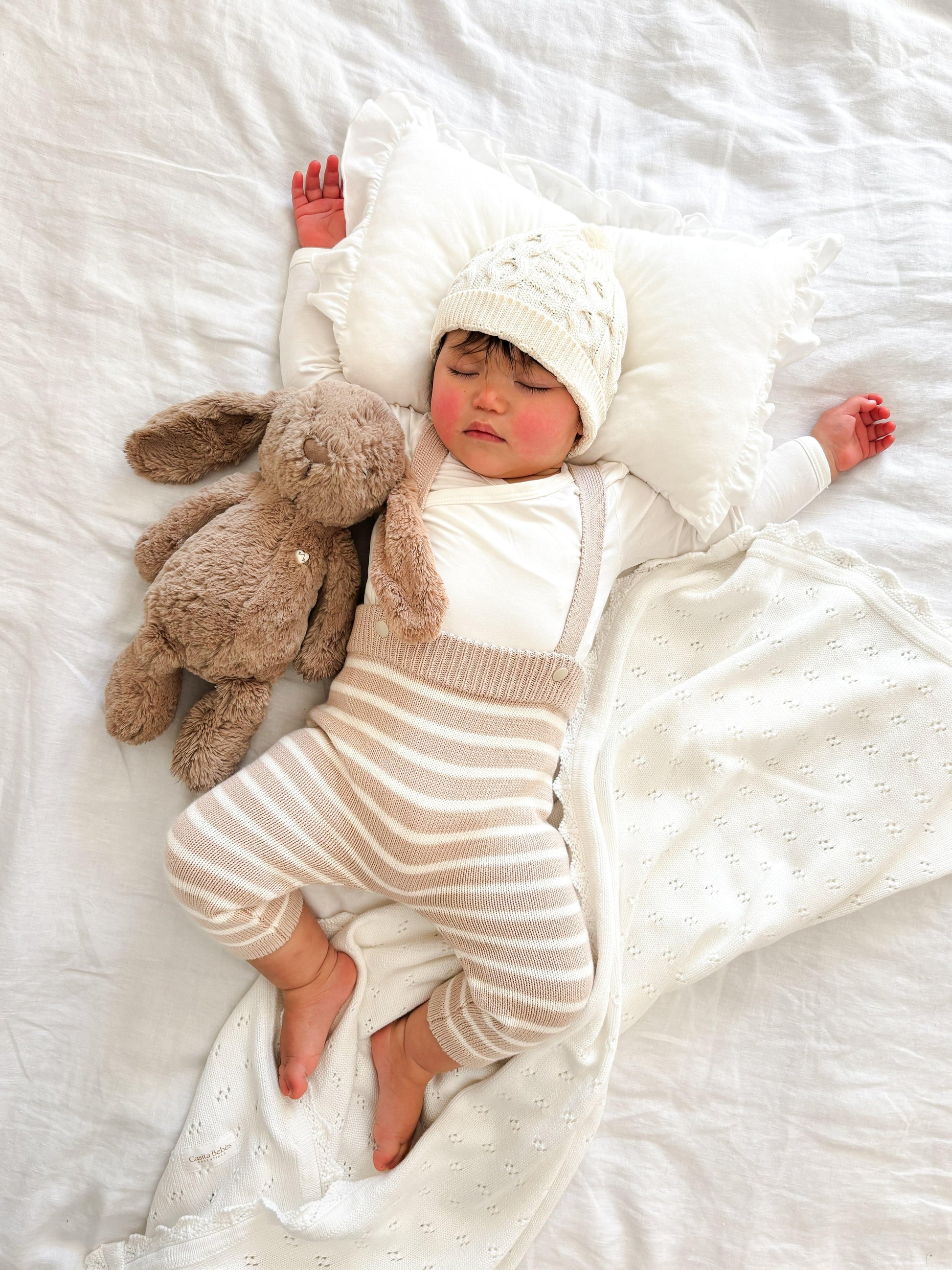 Baby wearing organic Casita Bebes knitted overalls in cream and beige stripes, certified organic baby clothing.