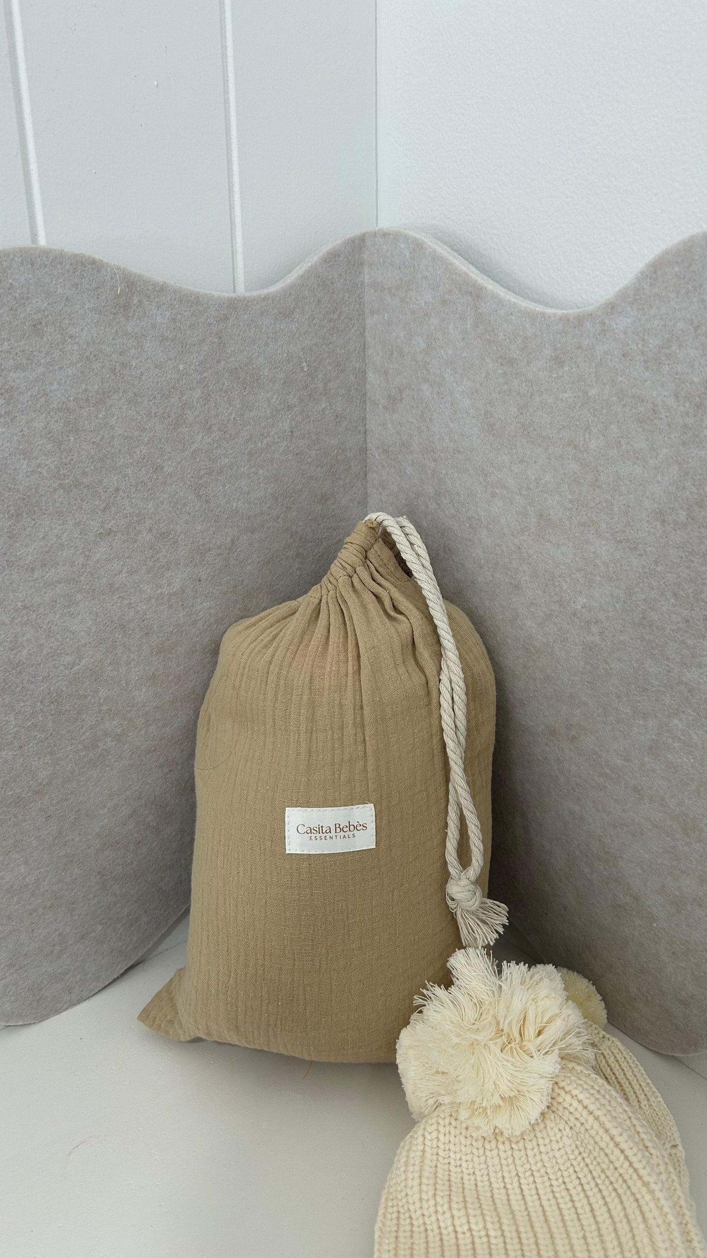 Organic baby essentials in a drawstring bag with pom-pom knit hat beside soft gray pillows