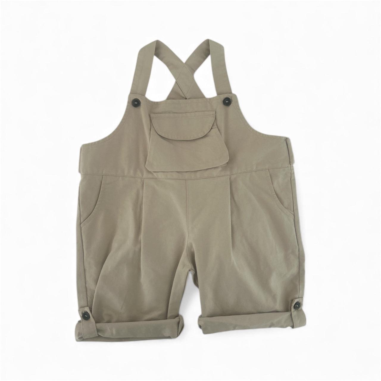 Beige organic cotton toddler overalls with front pocket and buttoned rolled cuffs.
