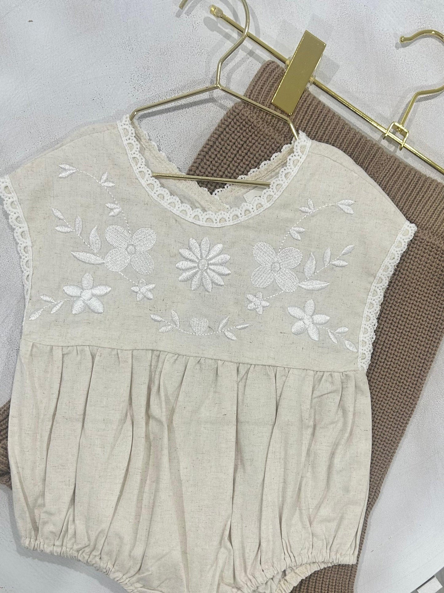 Organic cotton baby romper with white floral embroidery and scalloped trim, short sleeves.