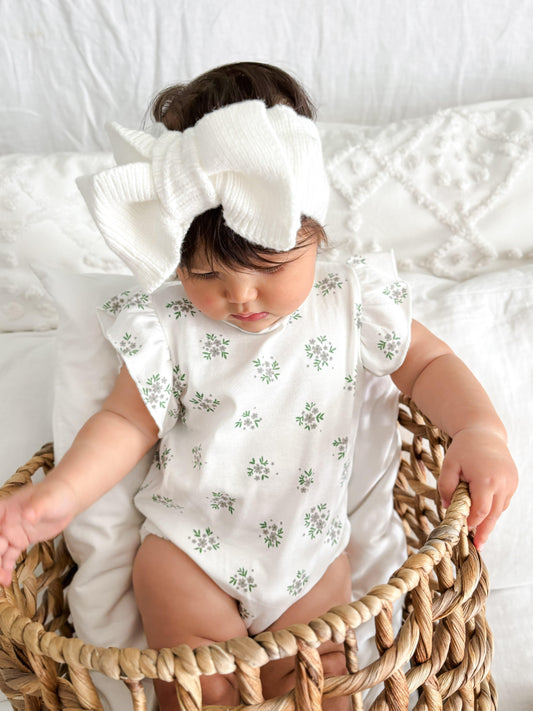 Baby wearing organic white knitted bow from Casita Bebes with certified organic floral baby clothing.