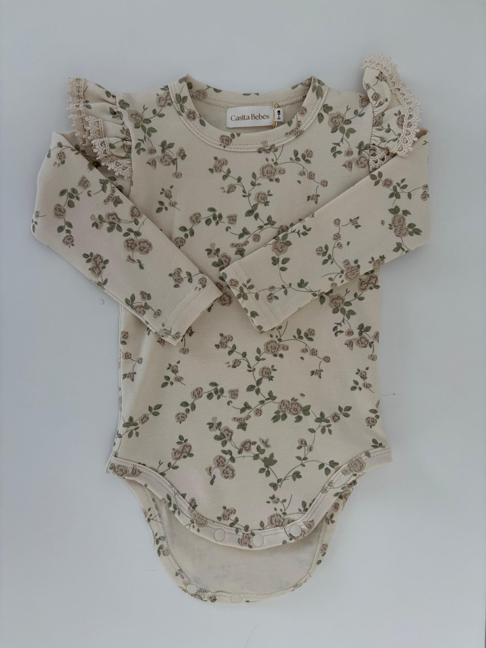 Organic cotton baby bodysuit with delicate floral print and ruffled shoulders by Casita Bebes.
