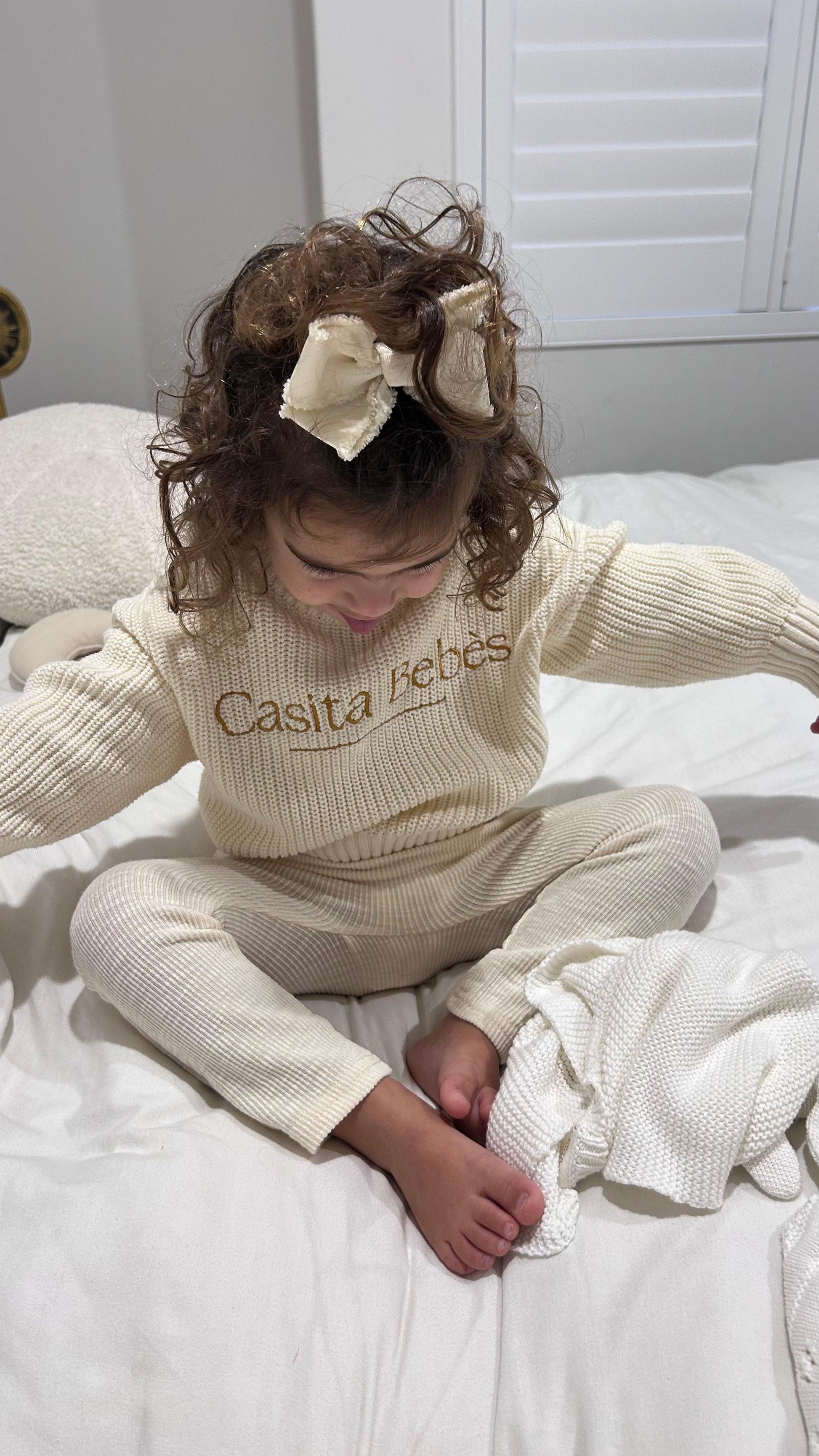 Baby wearing organic knit Essentīals Sweat set in cream with Casita Bebes logo embroidered on chest.