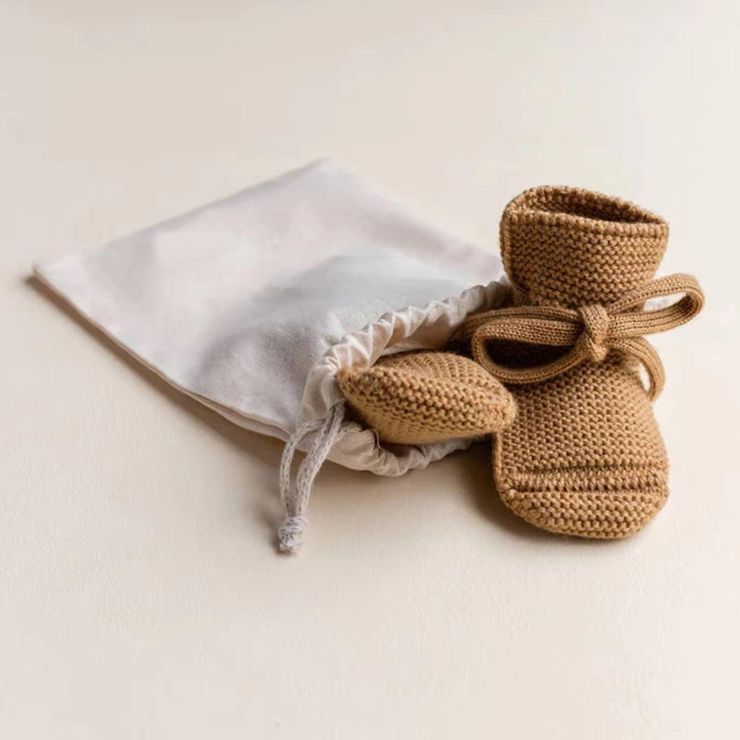 Organic dusty brown knit baby booties with ties beside white drawstring pouch, certified organic baby clothing by Casita.