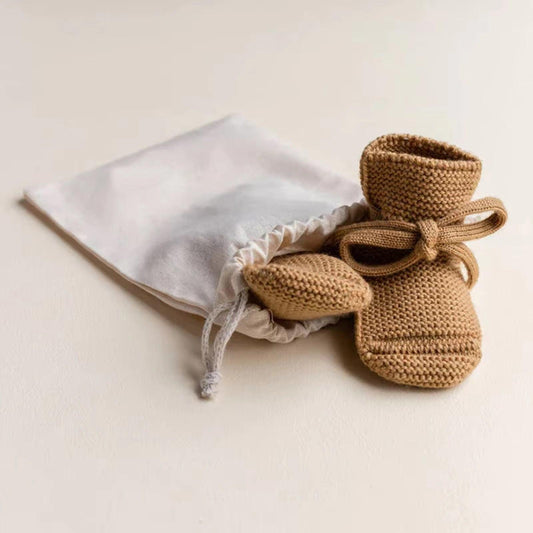 Organic dusty brown knit baby booties with ties beside white drawstring pouch, certified organic baby clothing by Casita.