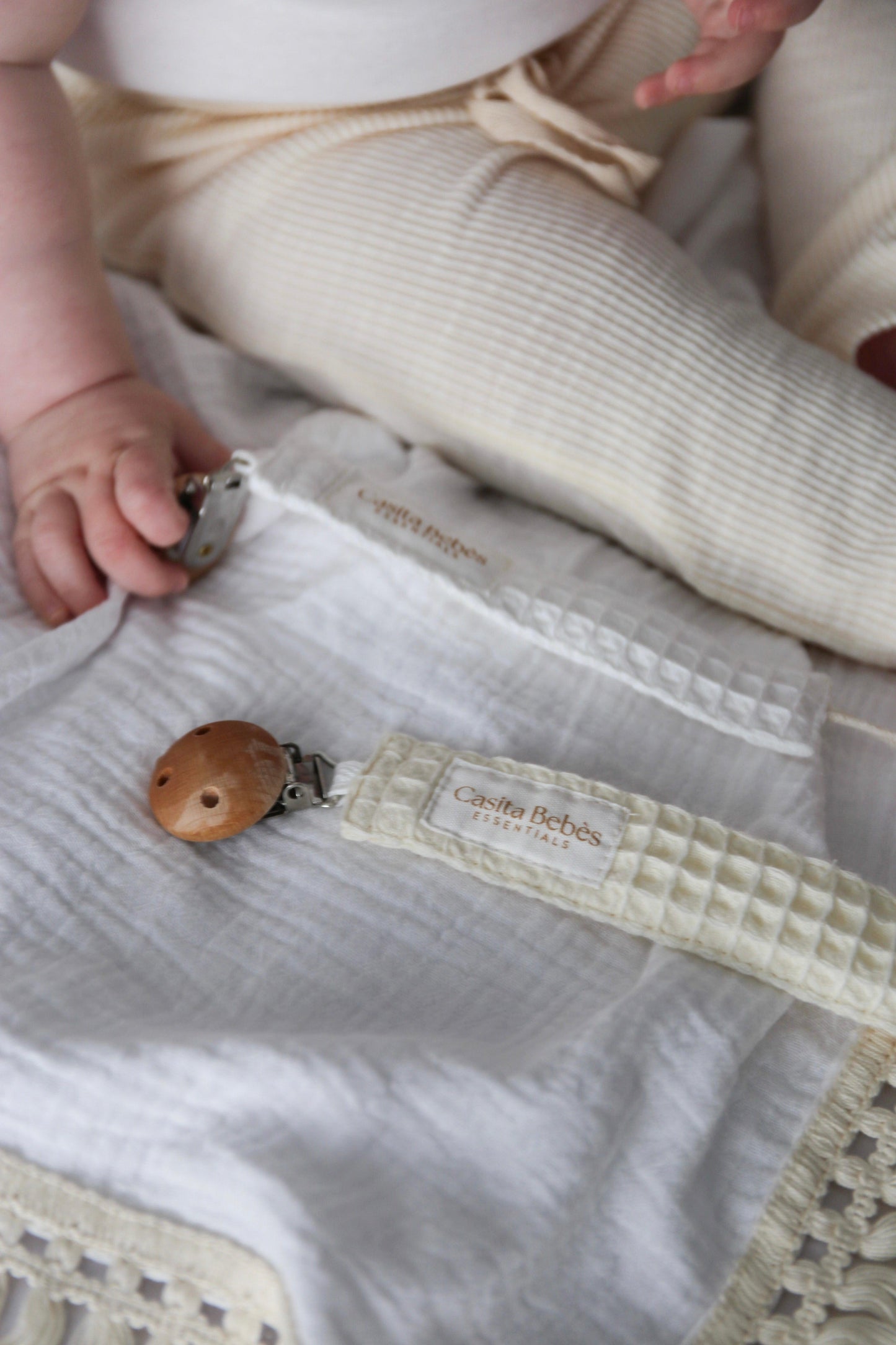 Baby holding wooden teether on organic cotton blanket with Casita Bebès Essentials tag
