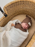 Baby sleeping in organic cotton wrap with plush duck, nestled in woven bassinet