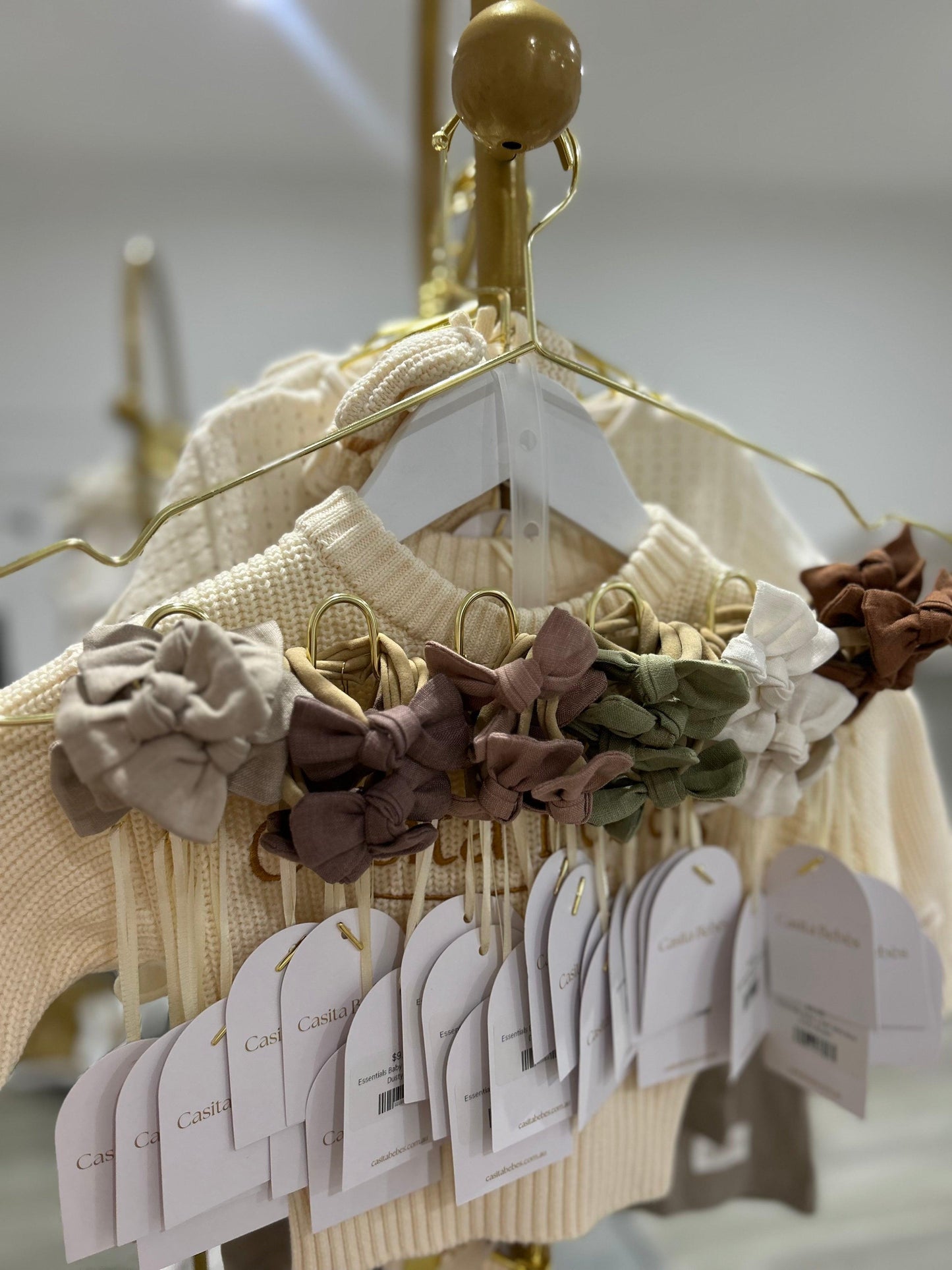 Soft organic baby hair ties in neutral tones, displayed on gold hangers with knitwear, perfect for everyday essentials.
