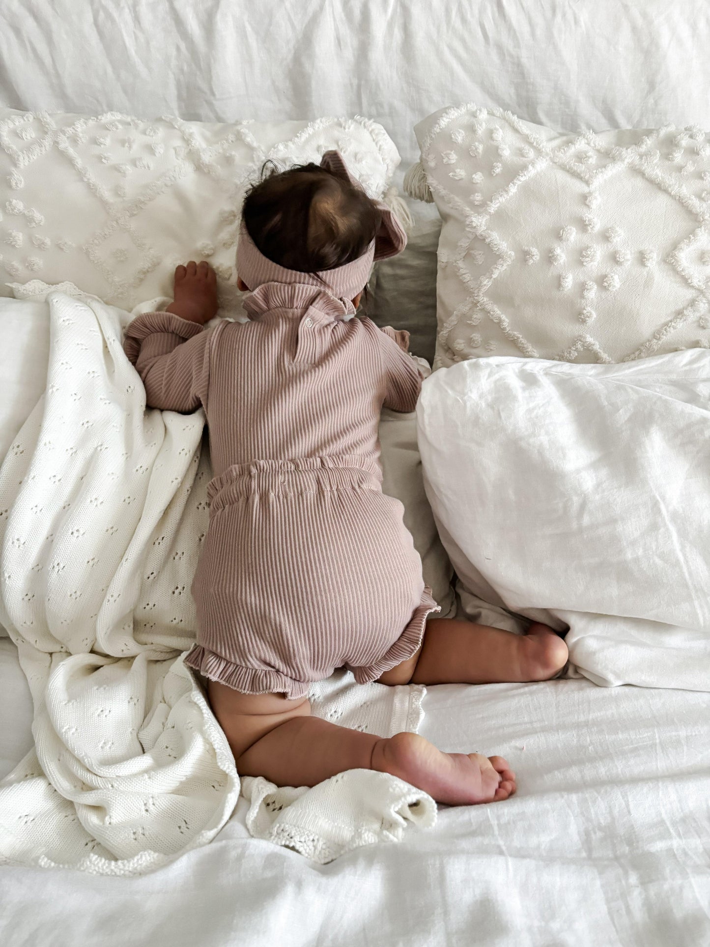 Baby wearing dusty pink ribbed organic cotton onesie with bow, Casita Bebes certified organic baby clothing.
