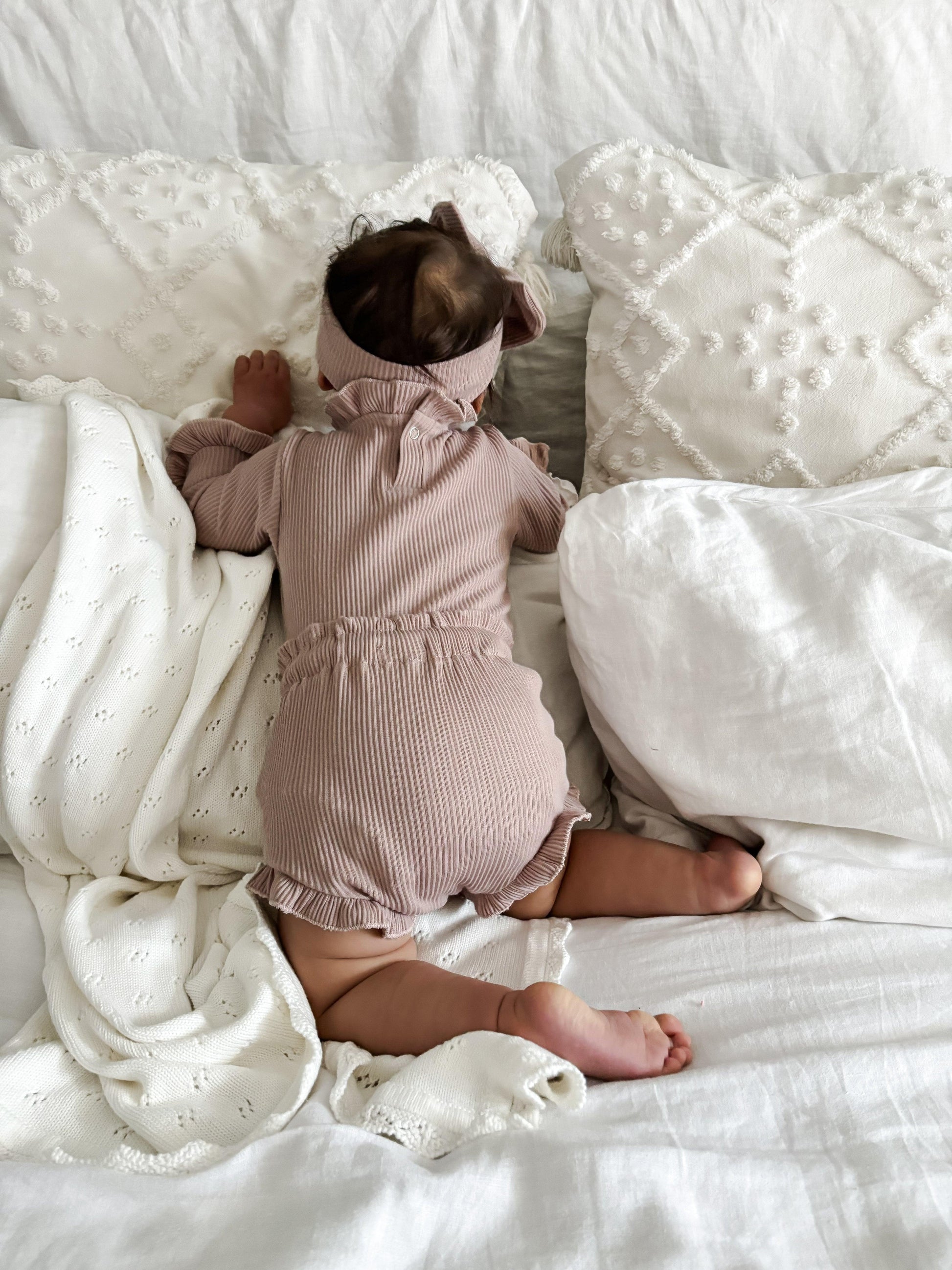 Baby wearing dusty pink ribbed organic cotton onesie with bow, Casita Bebes certified organic baby clothing.