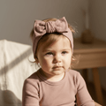 Baby in soft organic ribbed top and matching bow headband, gentle sunlight setting
