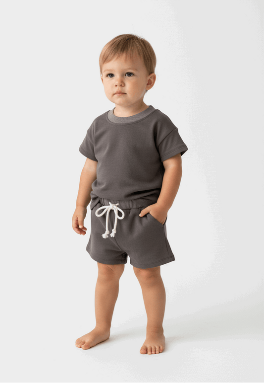 baby toddler standing with grey top and short set  on a white background