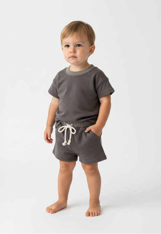 baby toddler standing with grey top and short set  on a white background